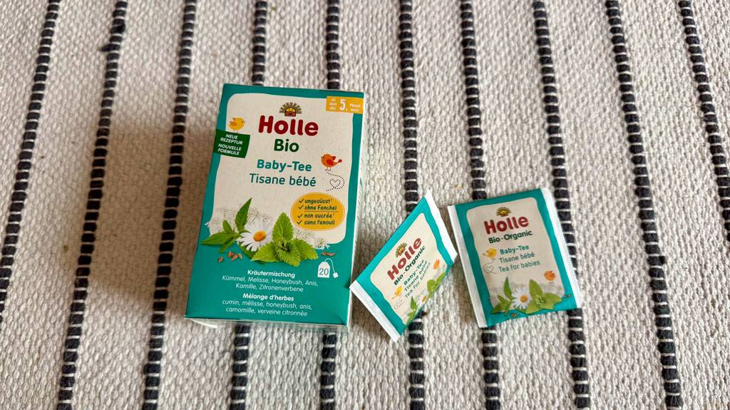 Blick von oben auf eine Packung Babytee, neben der zwei Beutel zum testen auf einem Teppichläufer liegen.