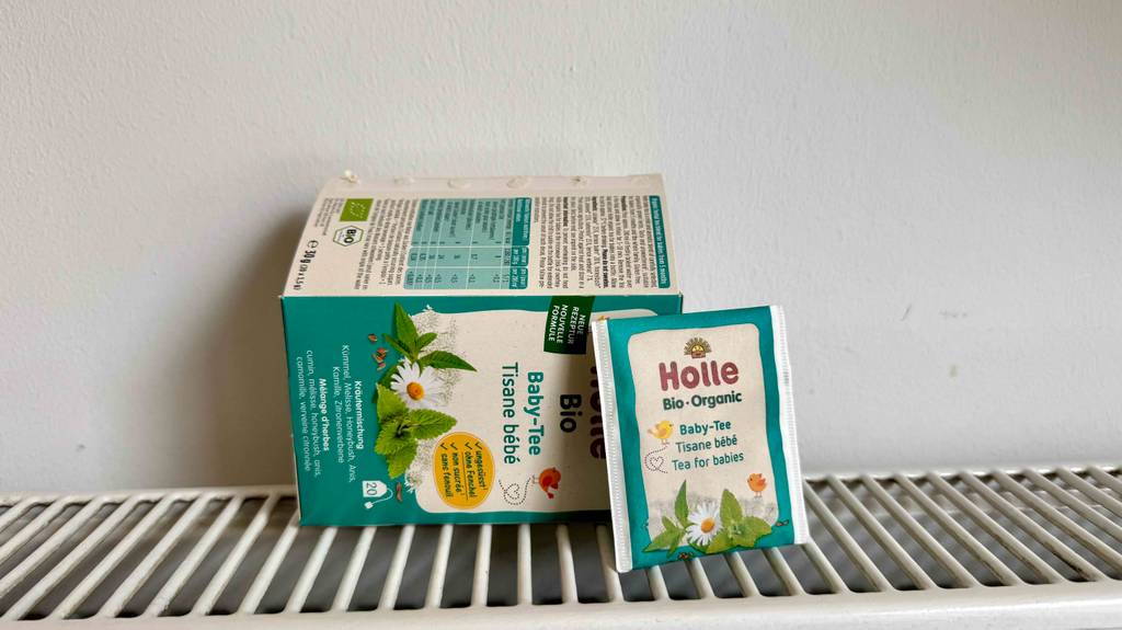Eine Packung Babytee liegt quer auf einem Gitterregal, davor ein Beutel zum testen.
