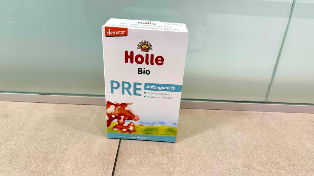 Vor einer Milchglaswand auf dem Boden steht eine Packung des getesteten Holle-Milchpulvers.