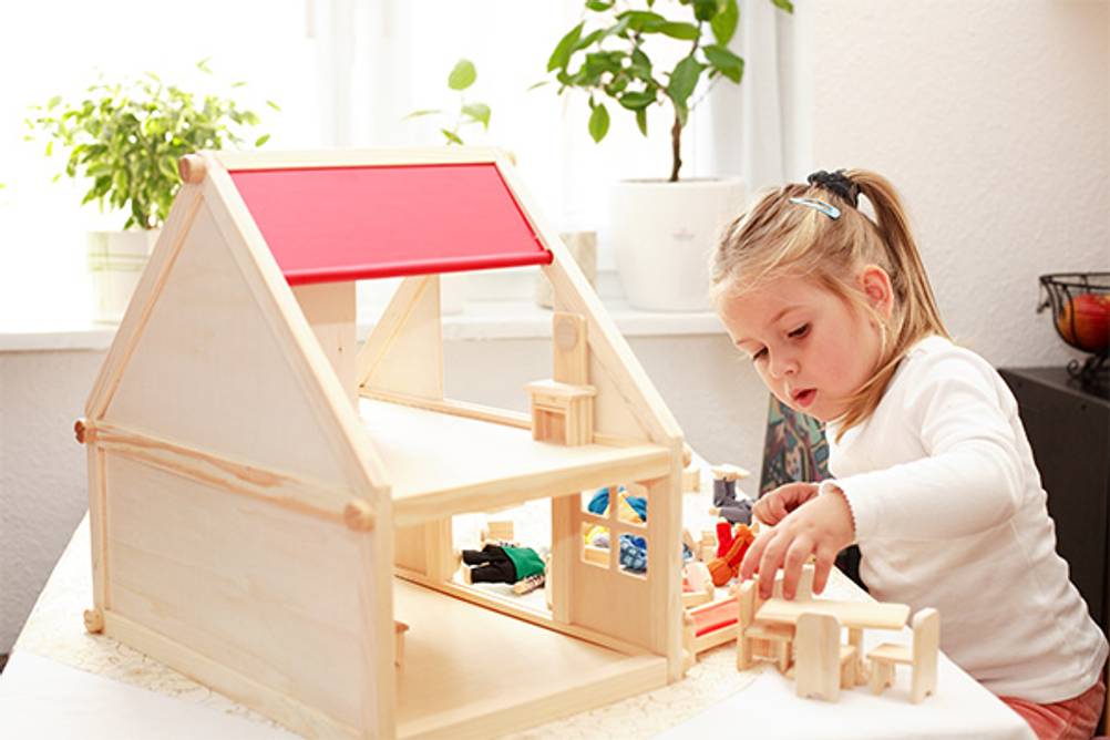 Puppenhaus aus Holz im Test: Ein Mädchen spielt mit einem kleinen Puppenhaus mit einem roten Dach.