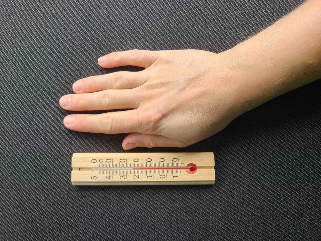 Ein Thermometer analog liegt zum testen neben einer flachen Hand.