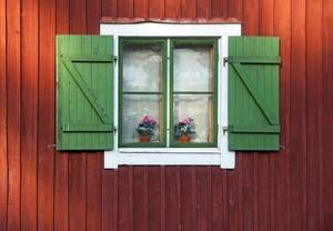 ein rotes Holzhaus mit einem weissen Fenster und gruenen Fensterlaeden