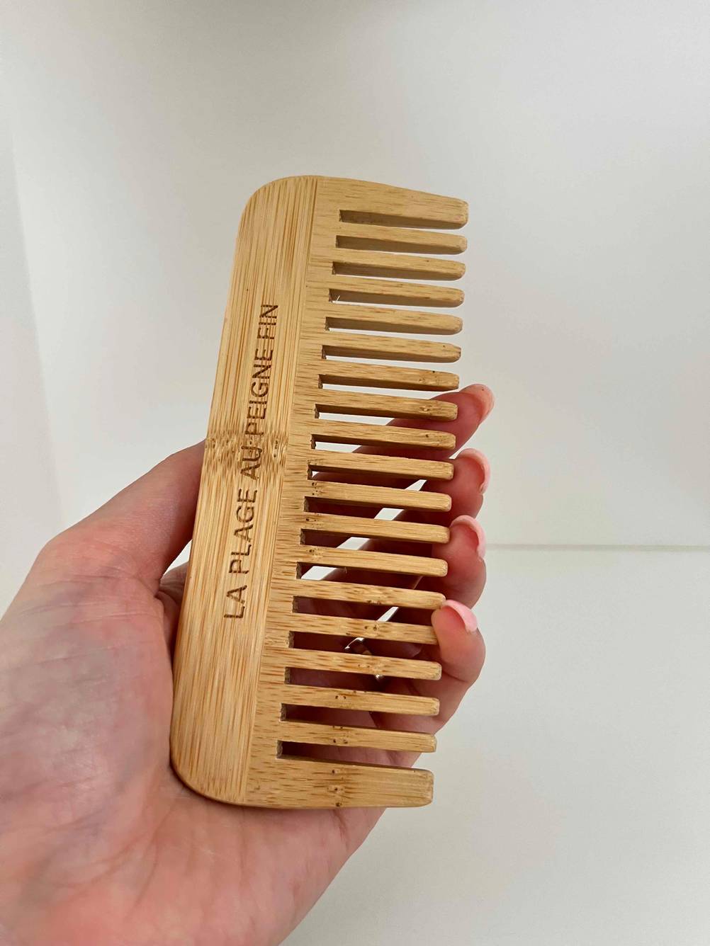 Eine Hand hält einen getesteten Kamm auf Holz vor einem weißen Hintergrund.