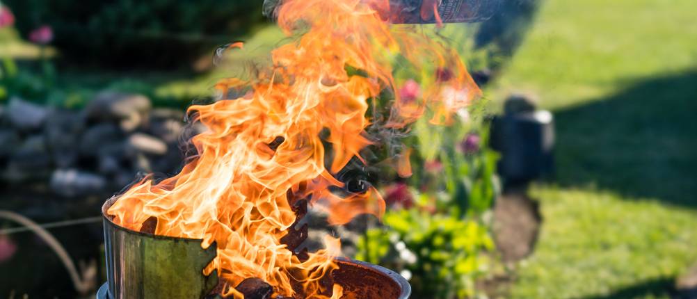 Die Holzkohle eines Holzkohlegrills wird mit einer Flüssigkeit übergossen, wodurch eine hohe Flamme entsteht.