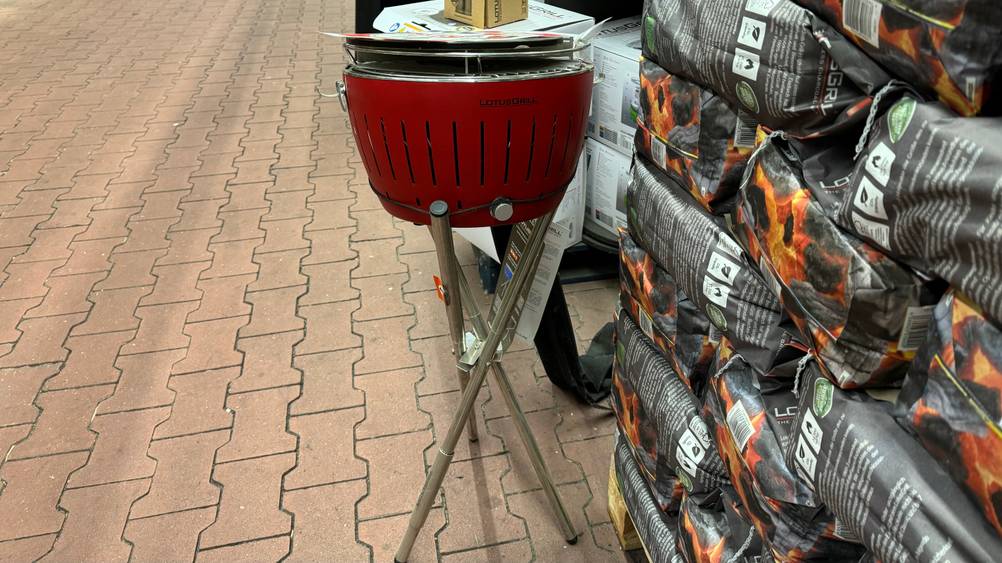 Vor mehreren Säcken Kohle steht ein getesteter Holzkohlegrill mit Aktivbelüftung.