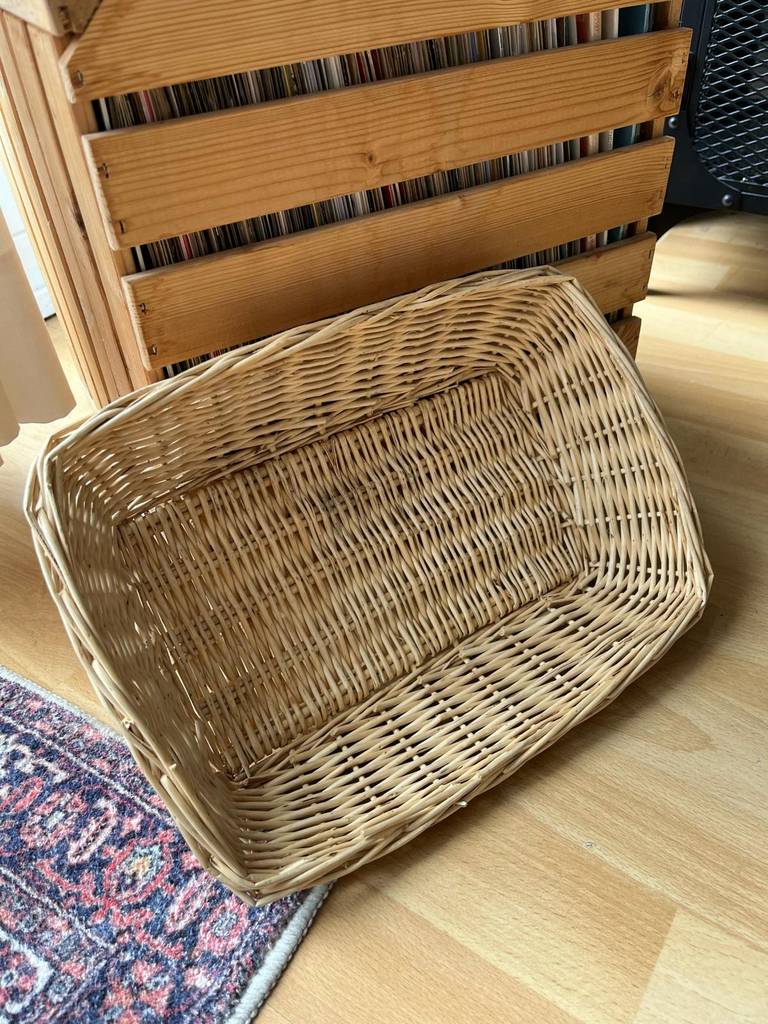 Holzkörbe im Test: Blick von seitlich oben auf ein geflochtenes, rechteckiges Modell aus hellem Holz, das an einer Holztruhe mit LPs lehnt.