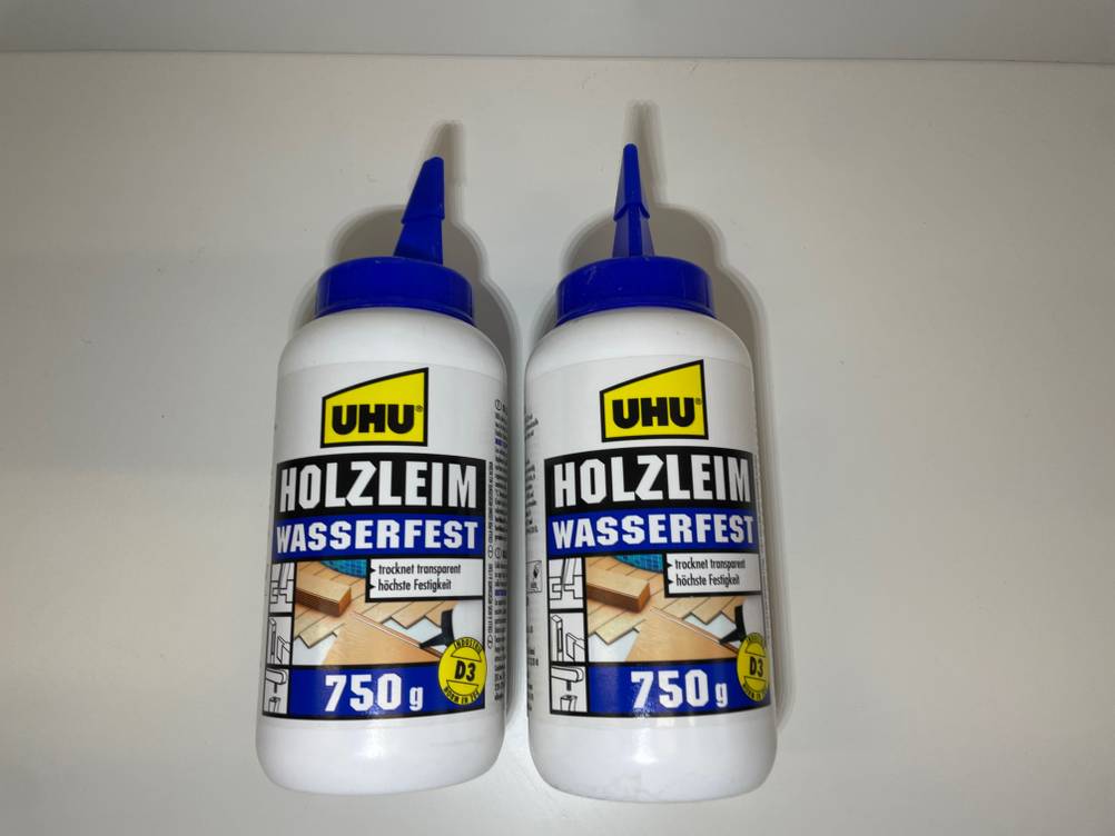 Zwei Tuben des getesteten Holzleims nebeneinander auf einer hellen Fläche liegend.