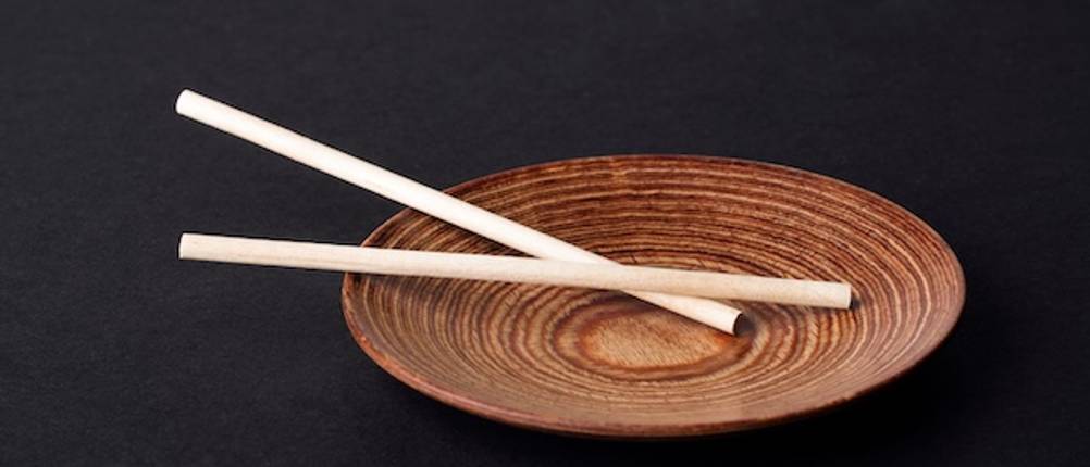 Flache Holzschale im Test: Auf dunklem Hintergrund eine flache dunkle Holzschale mit hellen Stäbchen.