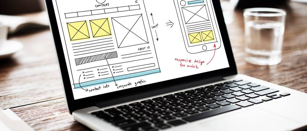 Auf einem Laptop ist die Skizze einer Webseite als Desktop- und Mobilversion abgebildet.