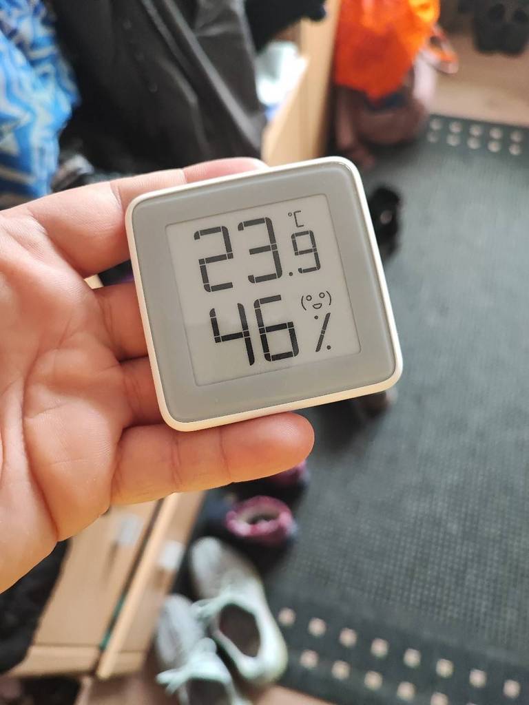 Hand hält ein Thermometer im Test von vorn in die Kamera innerhalb einer Umkleidekabine.