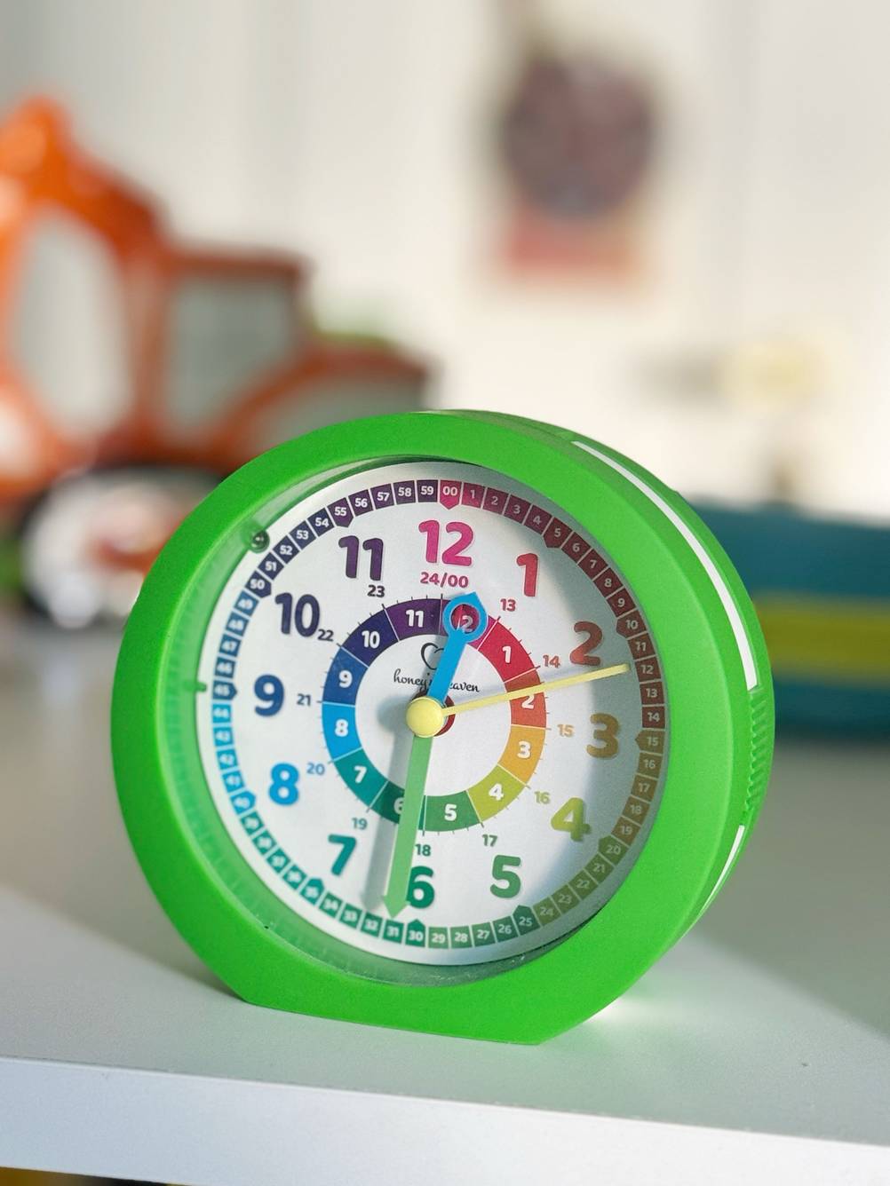 Ein grüner Kinderwecker mit buntem Ziffernblatt im Test steht auf einer weißen Fläche.