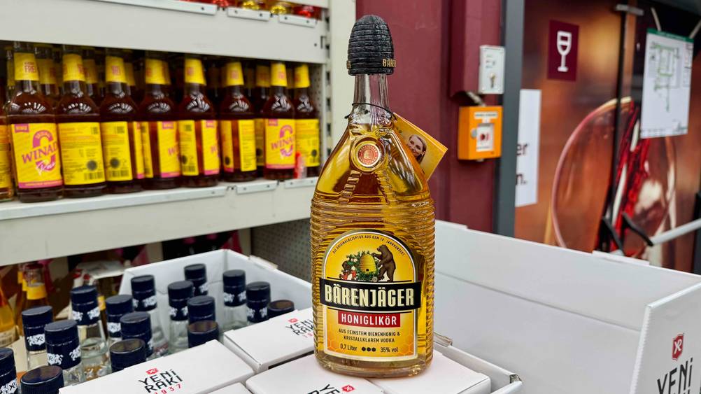 Eine Flasche des getesteten Honiglikörs auf einem Karton vor einem Regal.