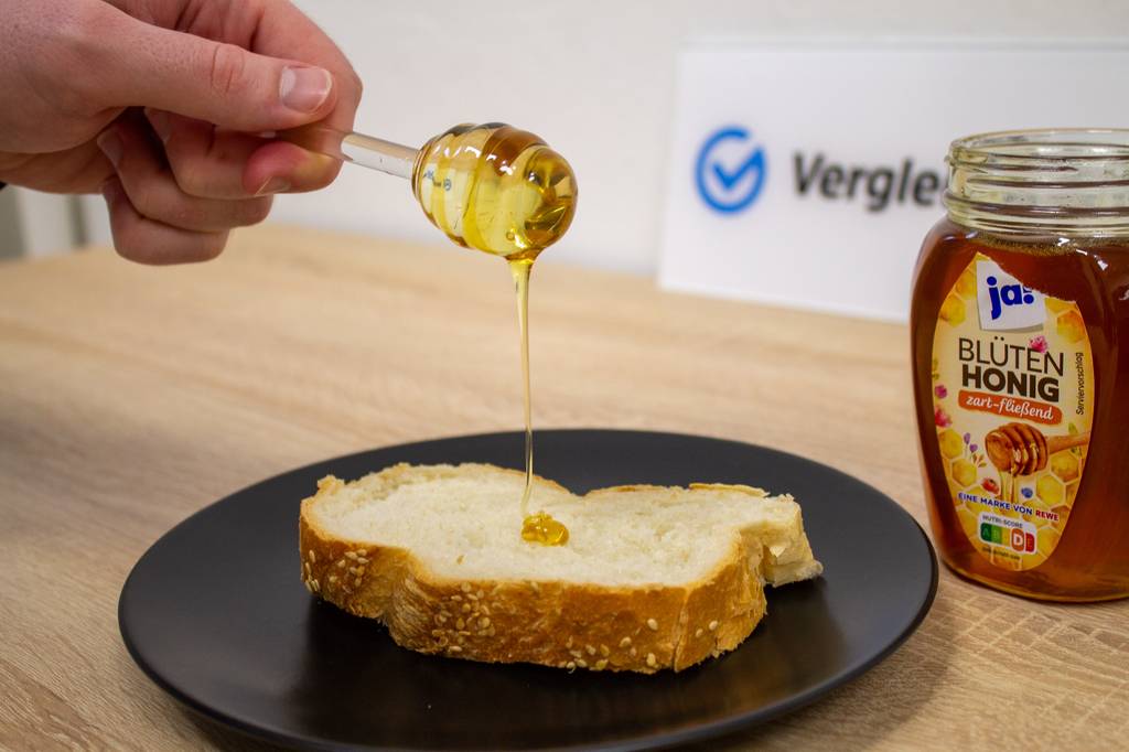 Honiglöffel-Test: Honiglöffel tropft Honig auf Brot.