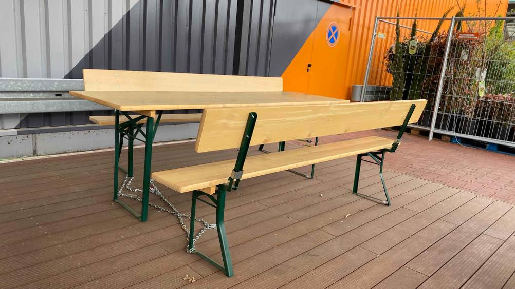 Eine Bierzeltgarnitur mit Lehne von hinten betrachtet steht mit einer Kette angekettet auf einer Terrasse.
