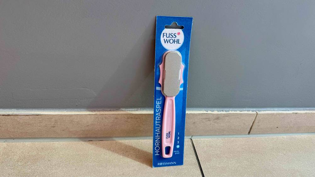 Vor einer grauen Wand am Boden steht ein getesteter Hornhautraspel in seiner Verpackung.