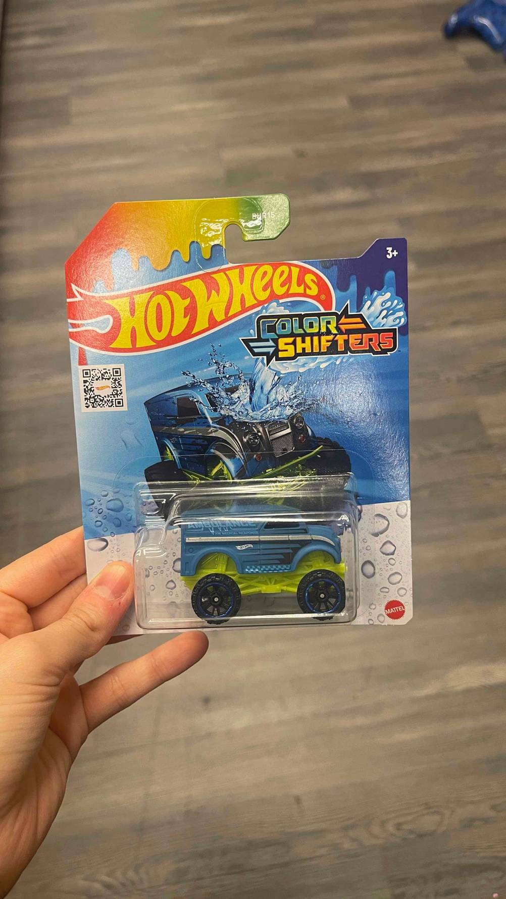 Eine Verpackung inklusive eines getesteten Hot-Wheels-Autos wird von einer Hand über einem Boden gehalten.