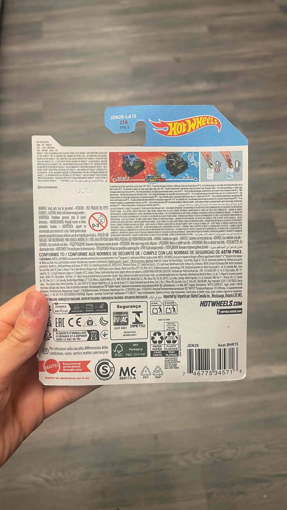 Eine Hand hält die Verpackung inklusive des Hot-Wheels-Autos im Test, mit Fokus auf die rückseitige Produktbeschreibung in die Kamera.