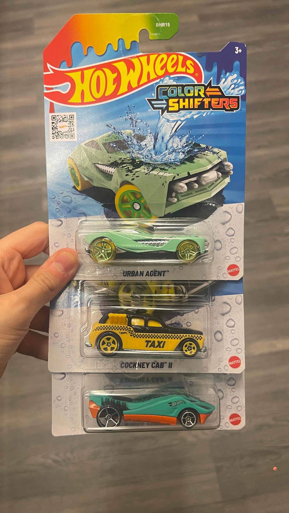 Drei getestete Hot-Wheels-Autos befinden sich in ihren Verpackungen übereinander in einer Hand.