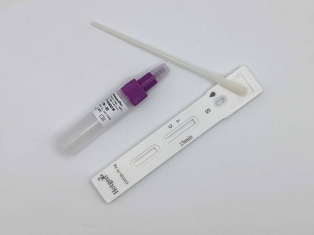 Ein Wattestäbchen ein Fläschchen und ein Teststreifen eines Coronavirus-Schnelltest-Sets auf einer hellen Oberfläche.