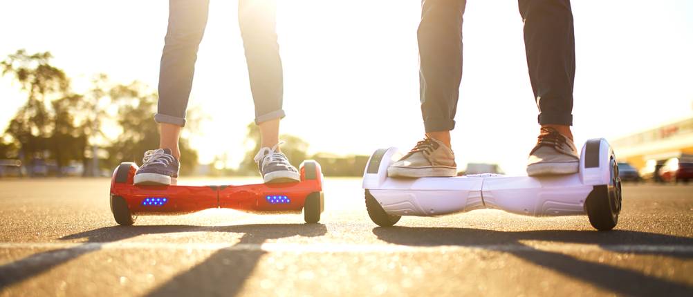 Hoverboard-Gelände-Test: Zwei Personen fahren auf einem Hoverboard auf einer sonnendurchfluteten Strasse. 