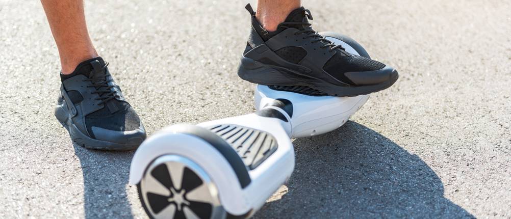 Hoverboard-Test: Nahaufnahme von Beinen, ein Fuß steht auf dem Hoverboard, der andere auf dem Asphalt