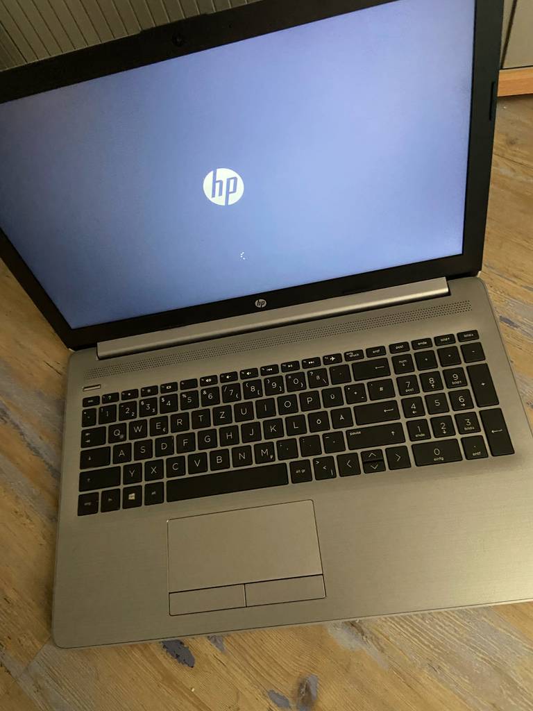 Der getestete Windows-10-Laptop steht geöffnet mit eingeschaltetem Bildschirm auf einem Holztisch.