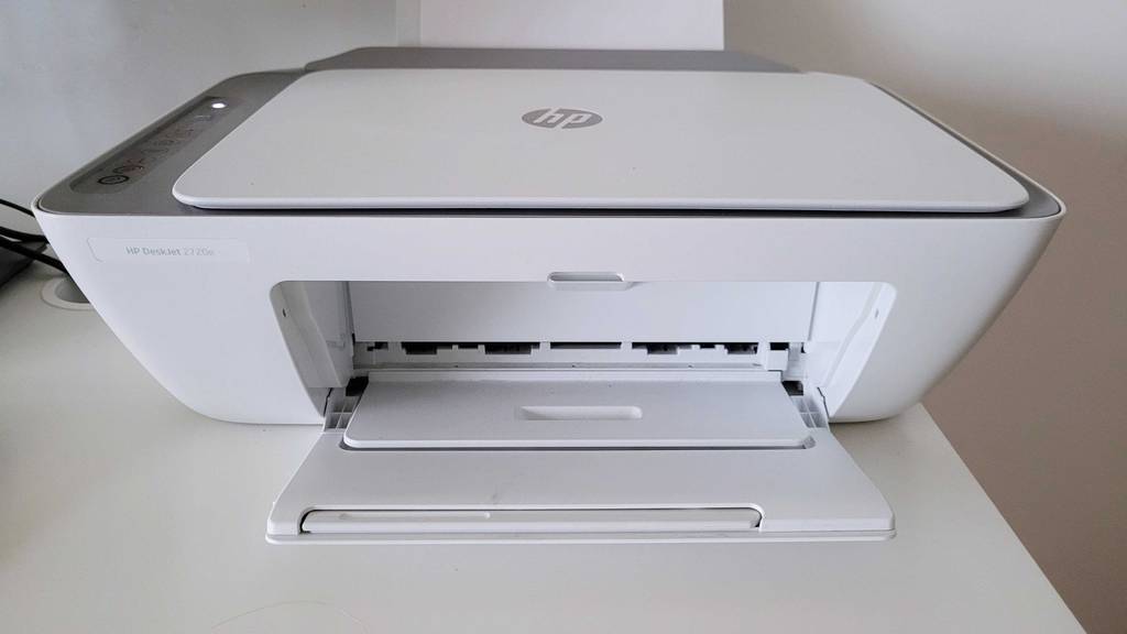 Gesamtansicht von vorn eines weißen HP-Multifunktionsdruckers im Test, der mit geöffneter Blattausgabe auf einer weißen Oberfläche steht.