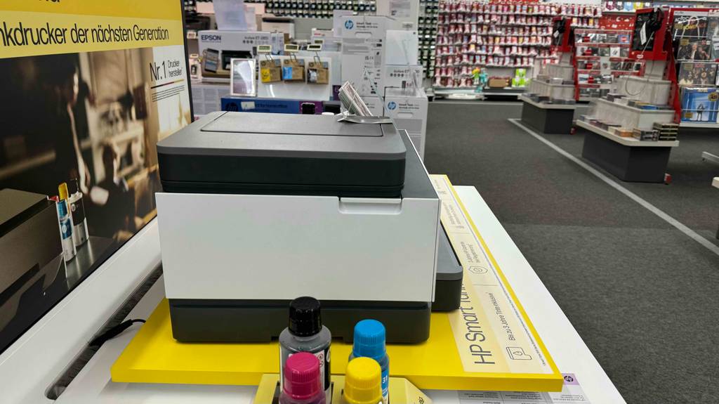 Seitenansicht auf einen getesteten Drucker mit Tank, der neben Flaschen mit nachfüllbarer Tinte in einem Geschäft ausgestellt ist.