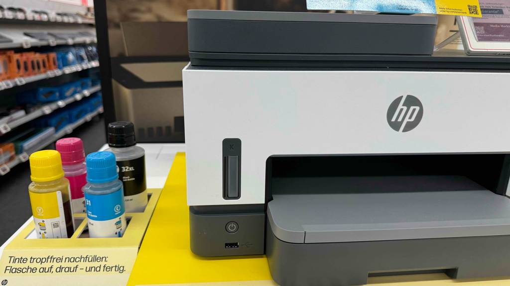Im Test: ein Drucker mit Tank der Marke HP steht von vorn betrachtet neben Tinten-Nachfüllflaschen in einem Geschäft.