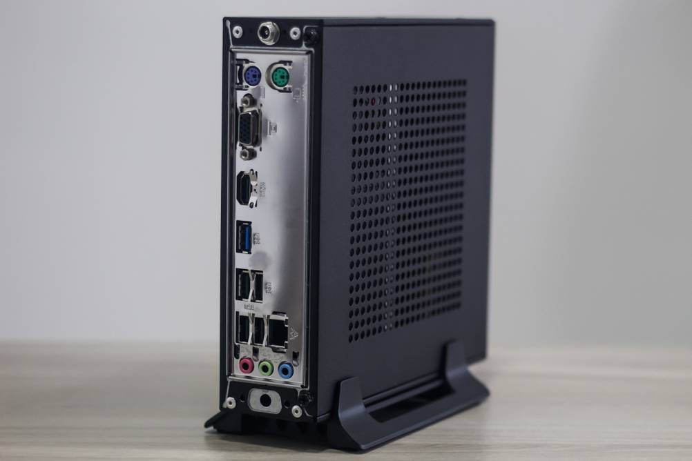 Lüfterloser Mini-PC im Test: Ein senkrecht in einer Halterung fixierter Mini-PC auf einem Tisch. Man sieht die Anschlüsse auf der Rückseite.