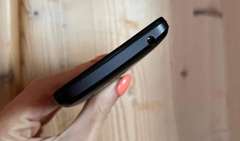 Hand hält schwarzes getestetes China-Handy mit Fokus auf den unteren äußeren Rand inklusive Kopfhörer-Buchse.