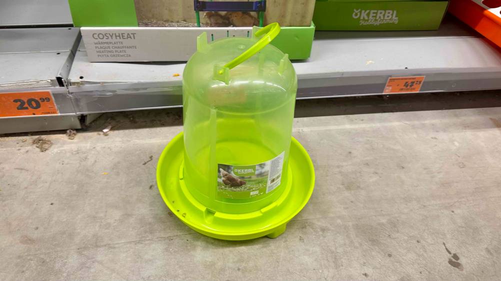 Eine Hühnertränke im Test von schräg oben vor einem Verkaufsregal.