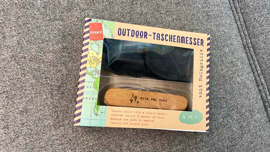 Ein getestetes Outdoormesser in seiner Originalverpackung auf einem grauen Stoff.