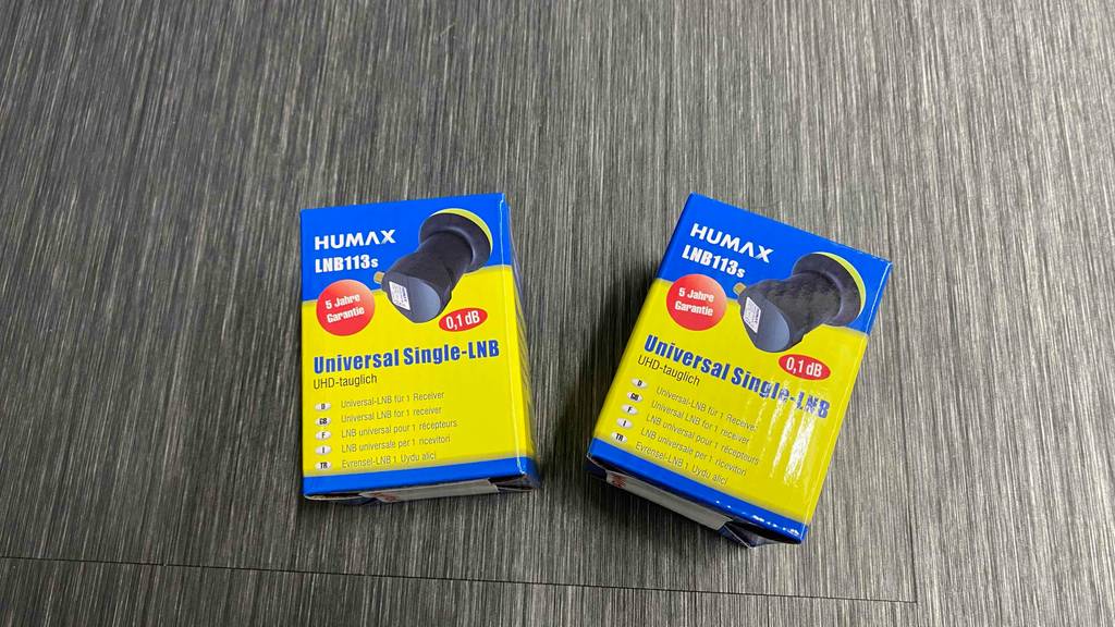 Zwei Packungen in Blau-gelb inklusive Single-Universal-LNB113s im Test befinden sich nebeneinander auf einem grauen Untergrund.