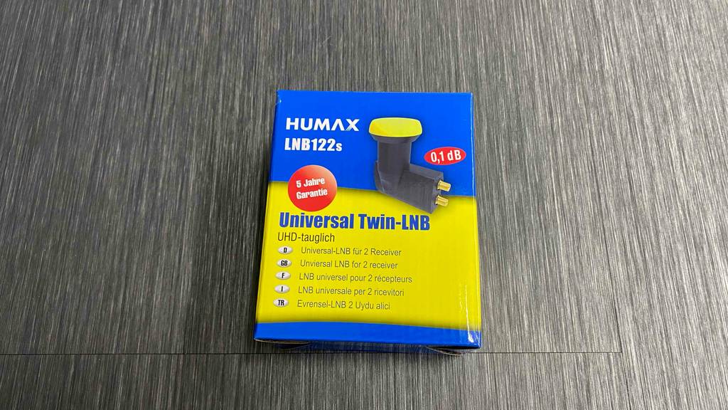 Eine Packung in Blau-gelb liegt inklusive getestetem Humax-Twin-LNB122s auf einem grauen Untergrund.
