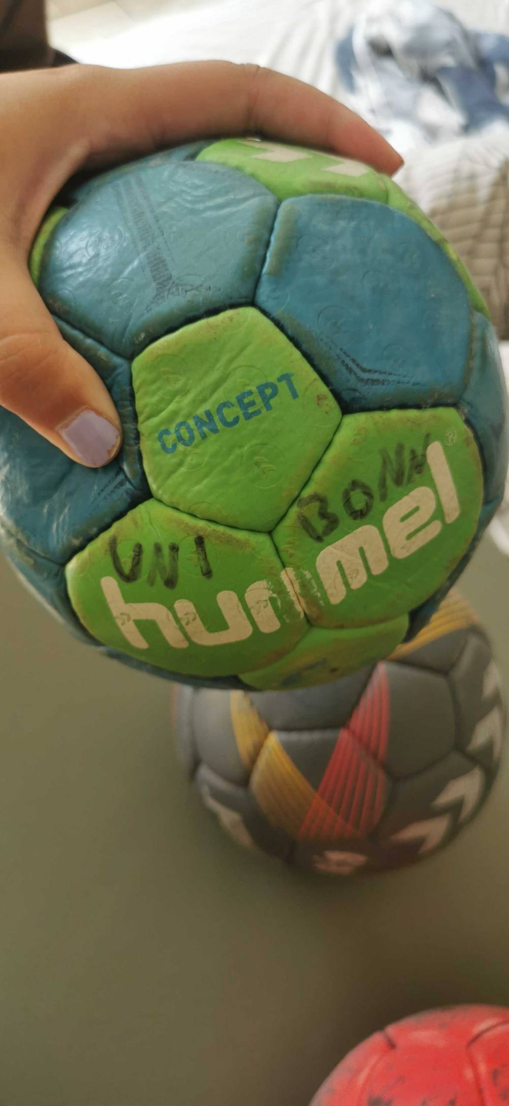 Handball im Test: Hand hält einen grün-blauen Ball mit mehreren Aufschriften.