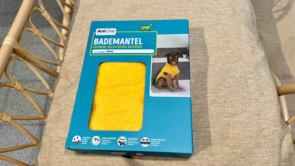 Ein gelber Hundebademantel im Test in seiner Originalverpackung auf einem beigen Polster.