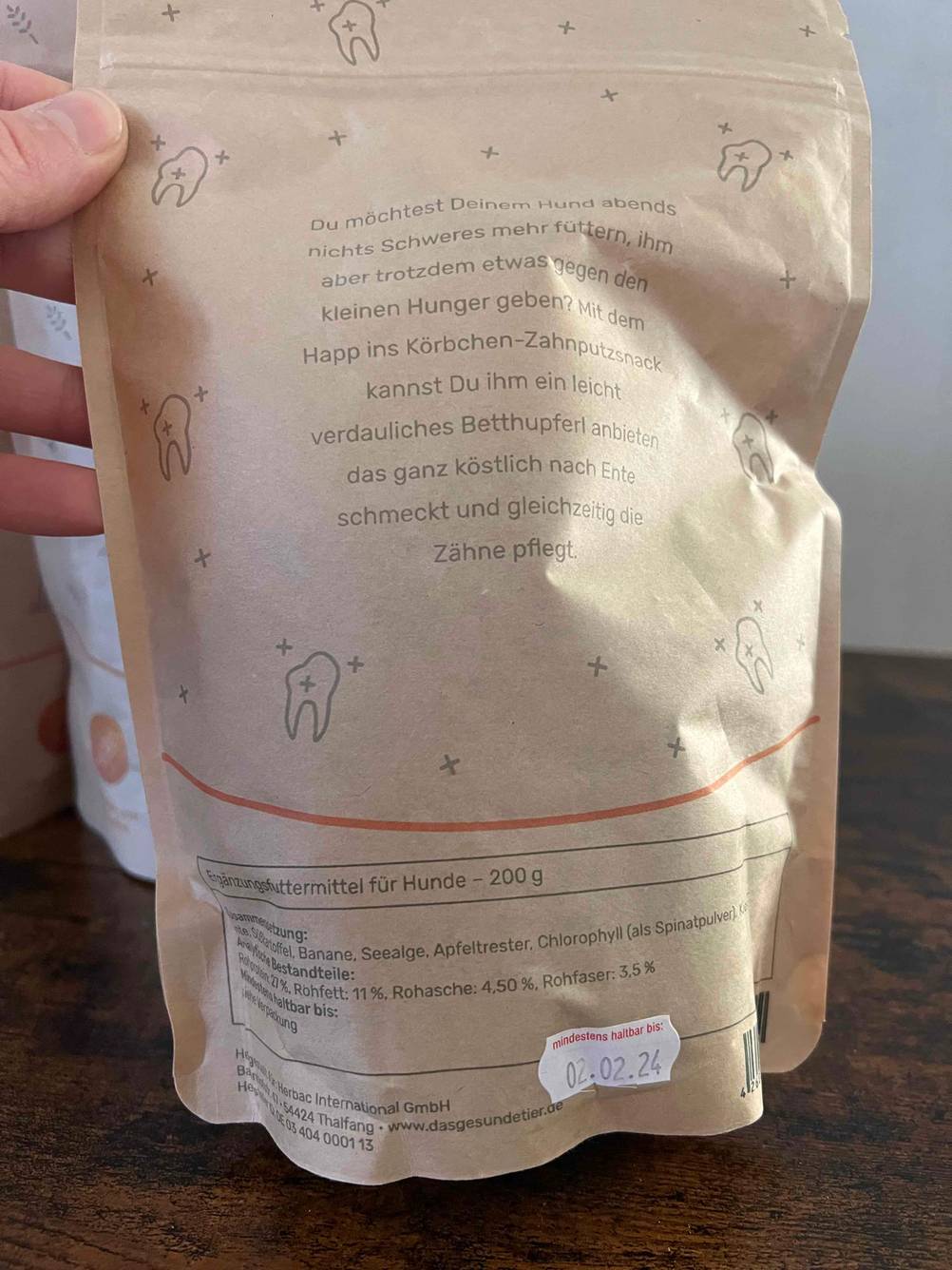In einer Hand befindet sich die Packung von getesteten Hundeleckerlies mit Nährwertangaben. 
