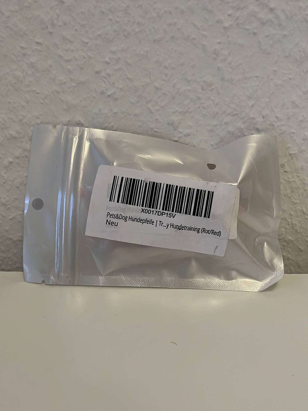 Die Rückseite einer verpackten Hundepfeife im Test vor einer hellen Wand.