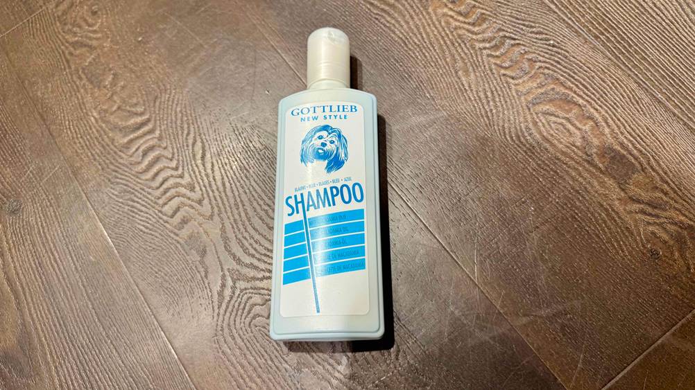 Eine Flasche des getesteten Hundeshampoo (weißes Fell) auf einem Holzboden liegend.