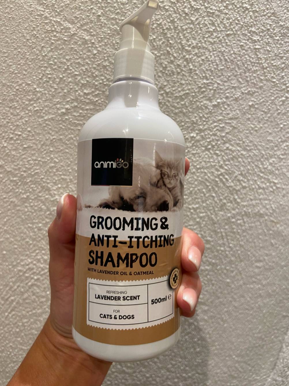 Eine Hand hält das getestete Hundeshampoo (weißes Fell) vor eine helle Wand.
