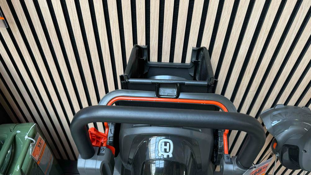 Nahaufnahme des Griffes eines Husqvarna-Rasenmäher im Test vor einer gestreiften Wand.