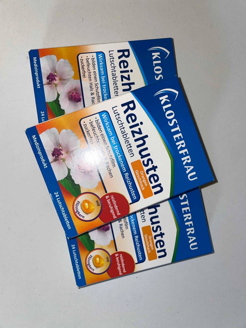 Auf einem Tisch befinden sich drei getestete Hustenbonbons-Packungen aufeinander gestapelt. 