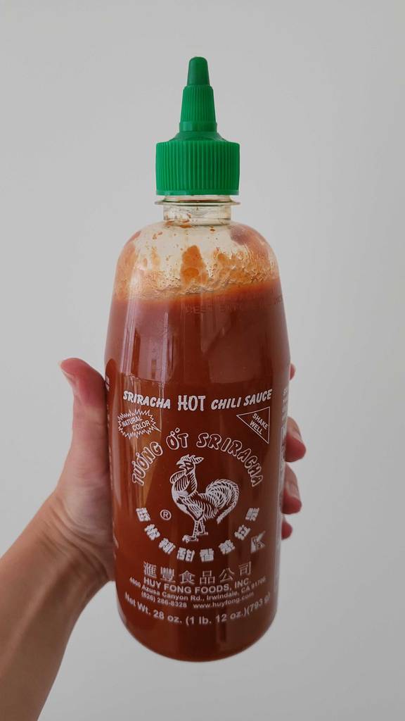 Chili-Soßen im Test: Eine Hand hält eine 500-g-Flasche mit roter Soße vor einer weißen Fläche.