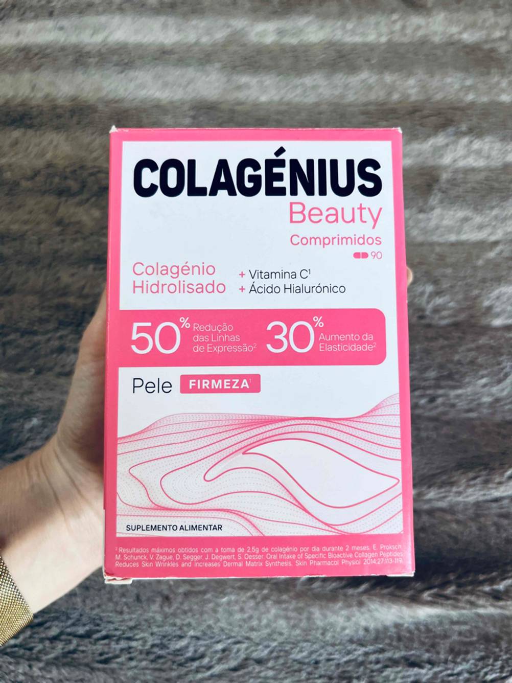 Eine Hand hält eine Packung der getesteten Hyaluron-Kollagen-Kapseln vor einen grauen Hintergrund.
