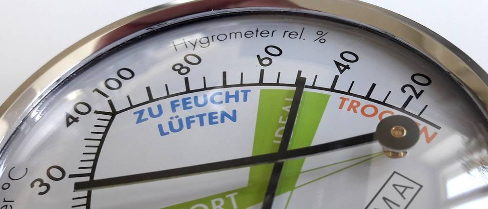 Nahaufnahme der Anzeige eines mechanischen Hygrometers mit grün markiertem Optimalbereich für Feuchte in der Luft.