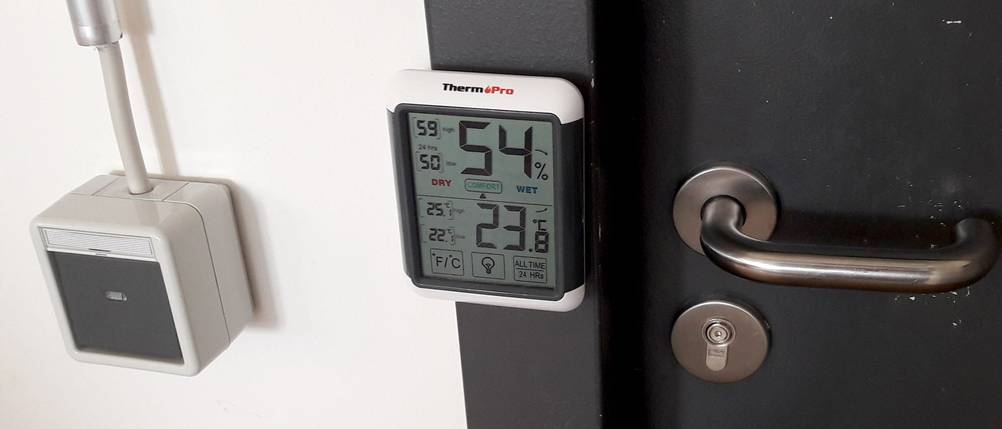 Ein Hygrometer mit Magnet am Rücken hängt an einem Türrahmen aus Metall.