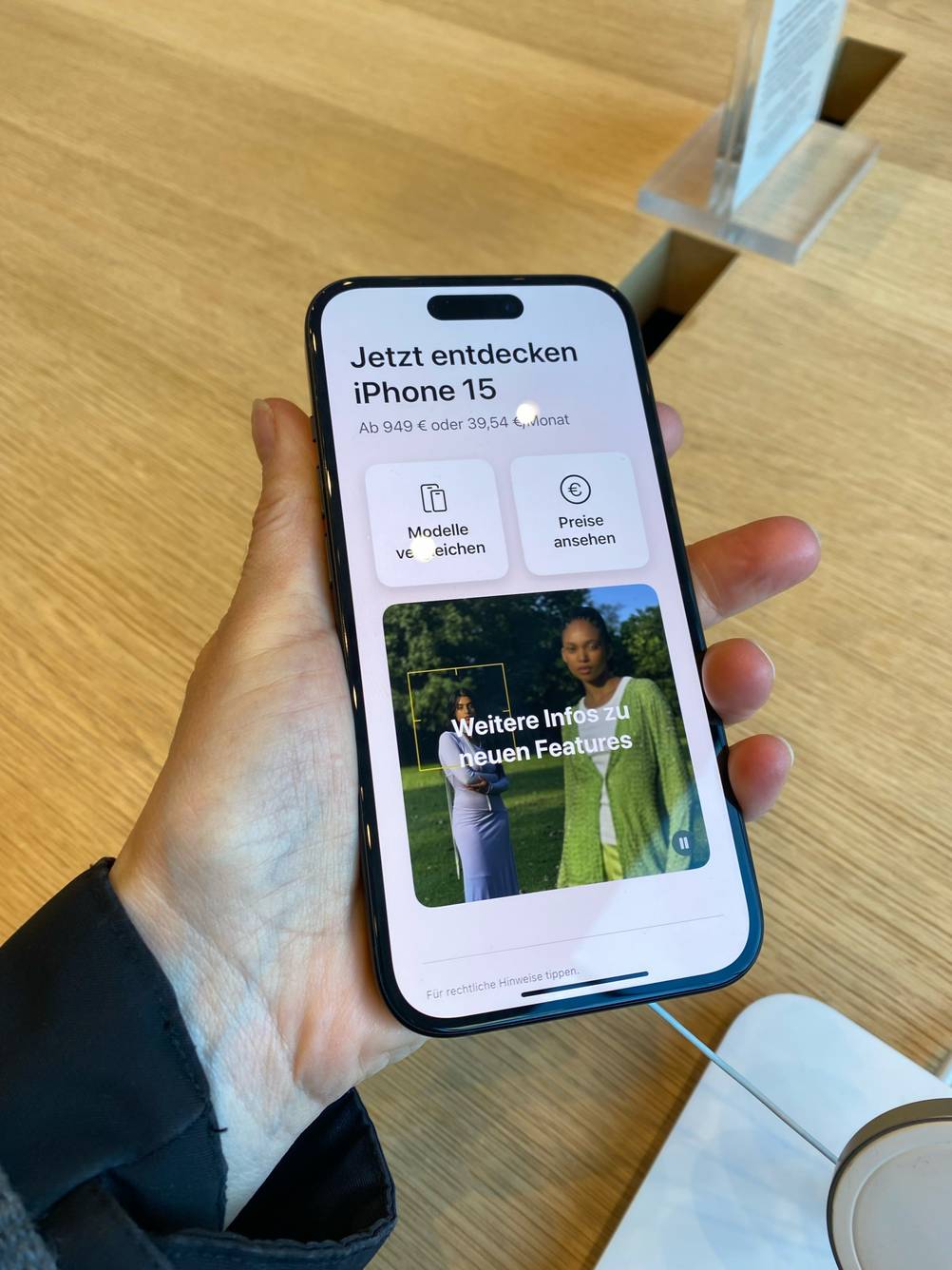 Handy mit guter Kamera im Test: Hand hält ein eingeschaltetes iPhone über einem Ausstellungstisch im Verkauf.