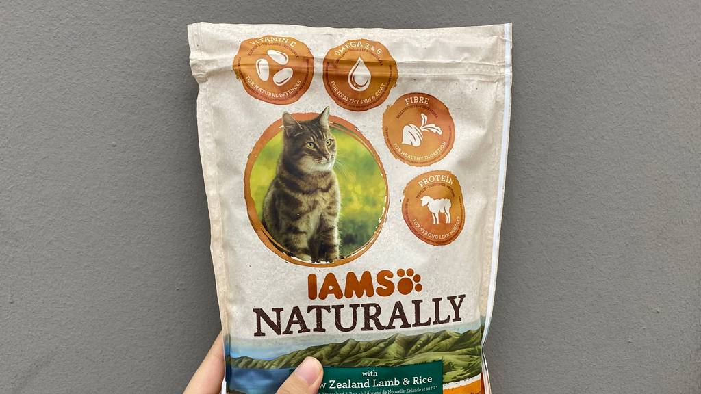 Im Test: Hand hält eine Packung IAMS Naturally Katzenfutter vor einem dunklen Hintergrund.