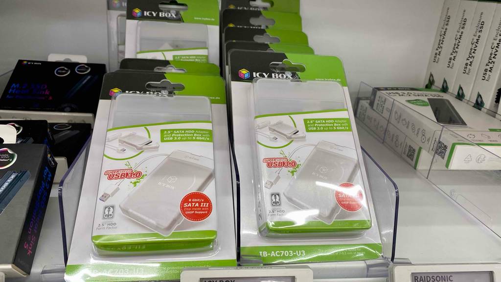 Mehrere weiß-grüne Verpackungen mit weißen 2,5-Zoll-Festplattengehäusen im Test liegen in einem weißen Regal im Geschäft.